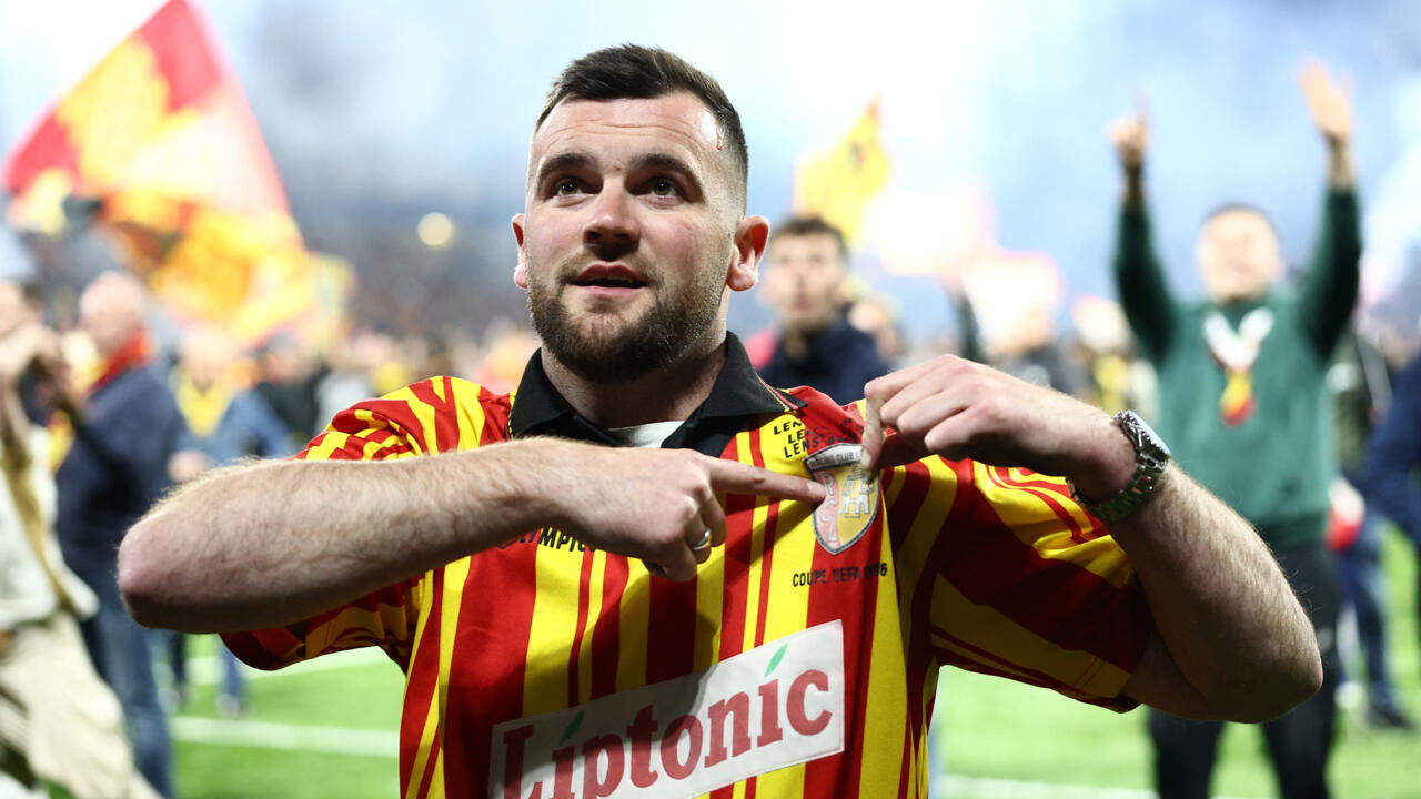 A supporter of Lens shows his jersey on the pitch after their team