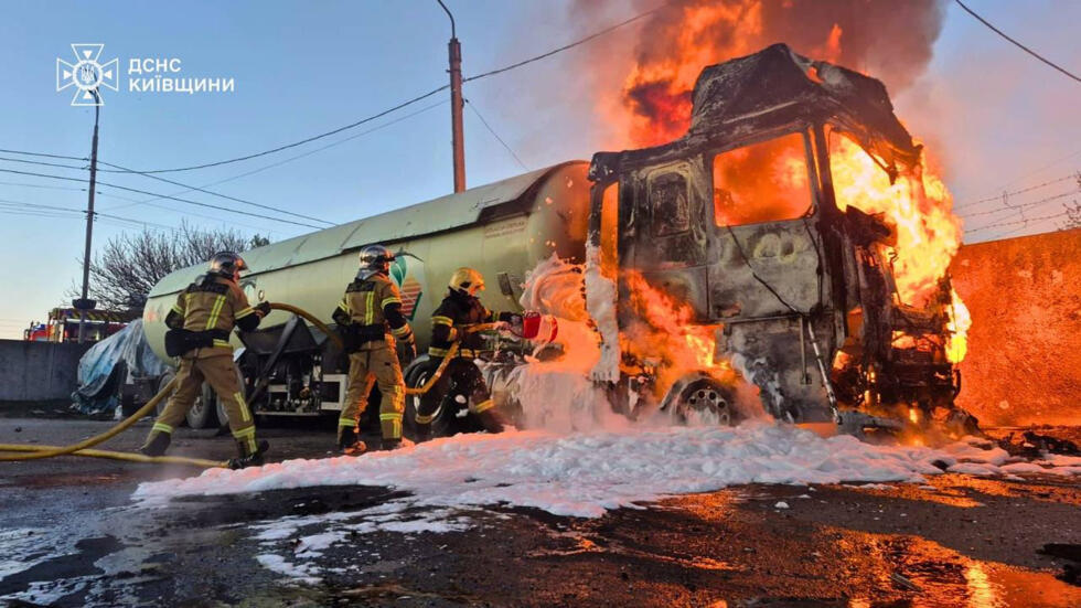 Ukrainian emergency services personnel work to extinguish a fire a vehicle following a Russian drone attack in Kyiv region.