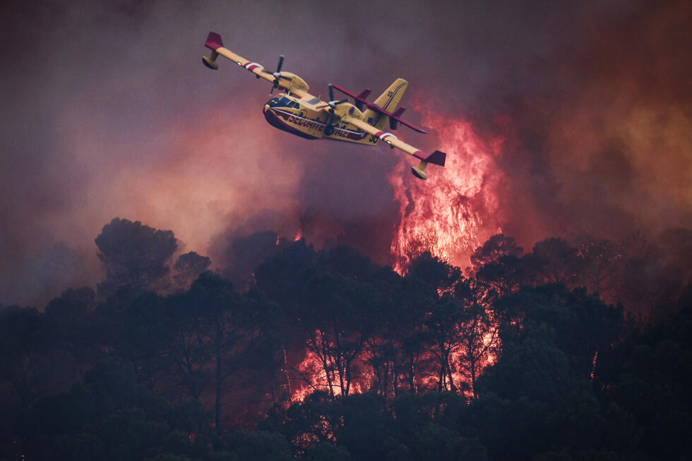 A French Civil Security Canadair CL-415 aircraft flies past flames burning a forest surrounding Cotignac, southeastern France during a wildfire.