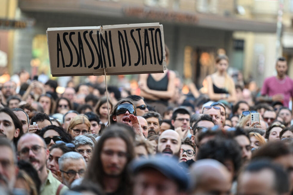 A protester holds a placard reading in Italian "State murderers" above a crowd during a protest following the death of Abderrahim Fakir