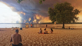 Beach goers rest on the beach of Moutchic on the shore of Lake Lacanau in southwestern France as clouds of smoke rise into the sky from the Gironde wildfire.