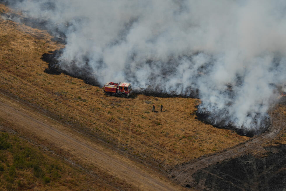 This aerial view, taken from a Civil Security helicopter, shows firefighters beside a fire truck working to bring under control a fire ravaging a field near Ares, southwestern France, on July 28, 2026.