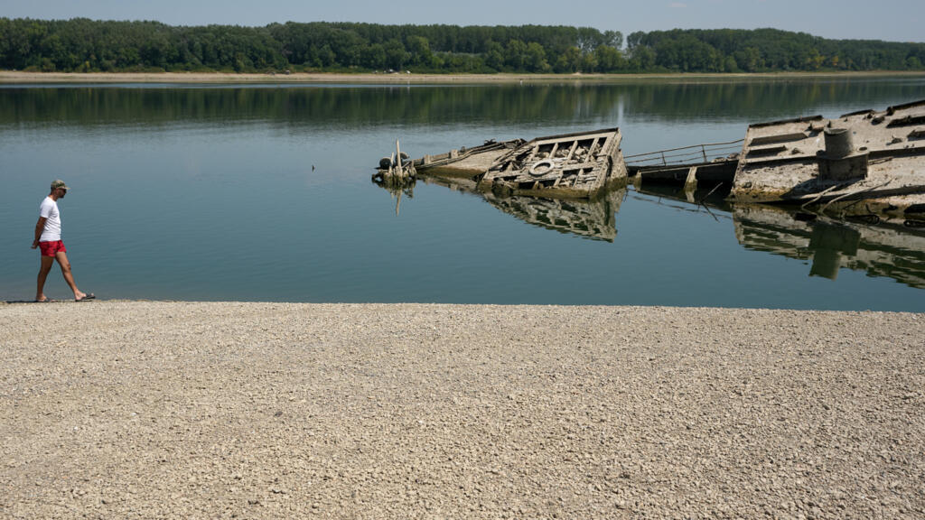 A man walks on the sandbank by the wreckage of a WWII German warship, emerged due to the drought, in front of Djerdap II, a large dam on the Danube River, between Romania and Serbia.