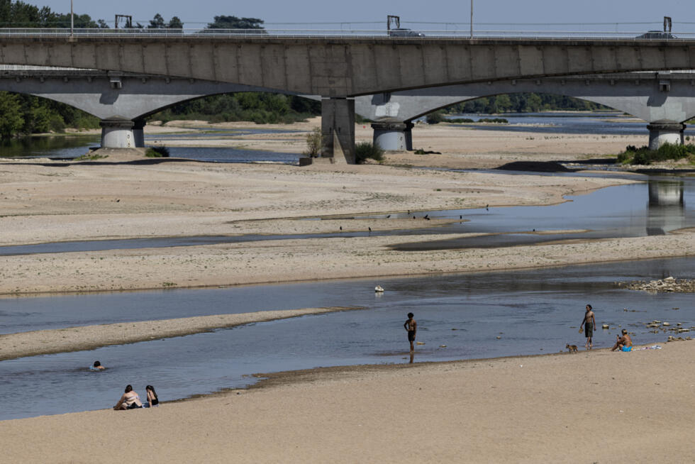 Visitors bathe and sit on the sand of the partially dry Loire riverbed with a bridge in the background in Orléans central France on July 22, 2026