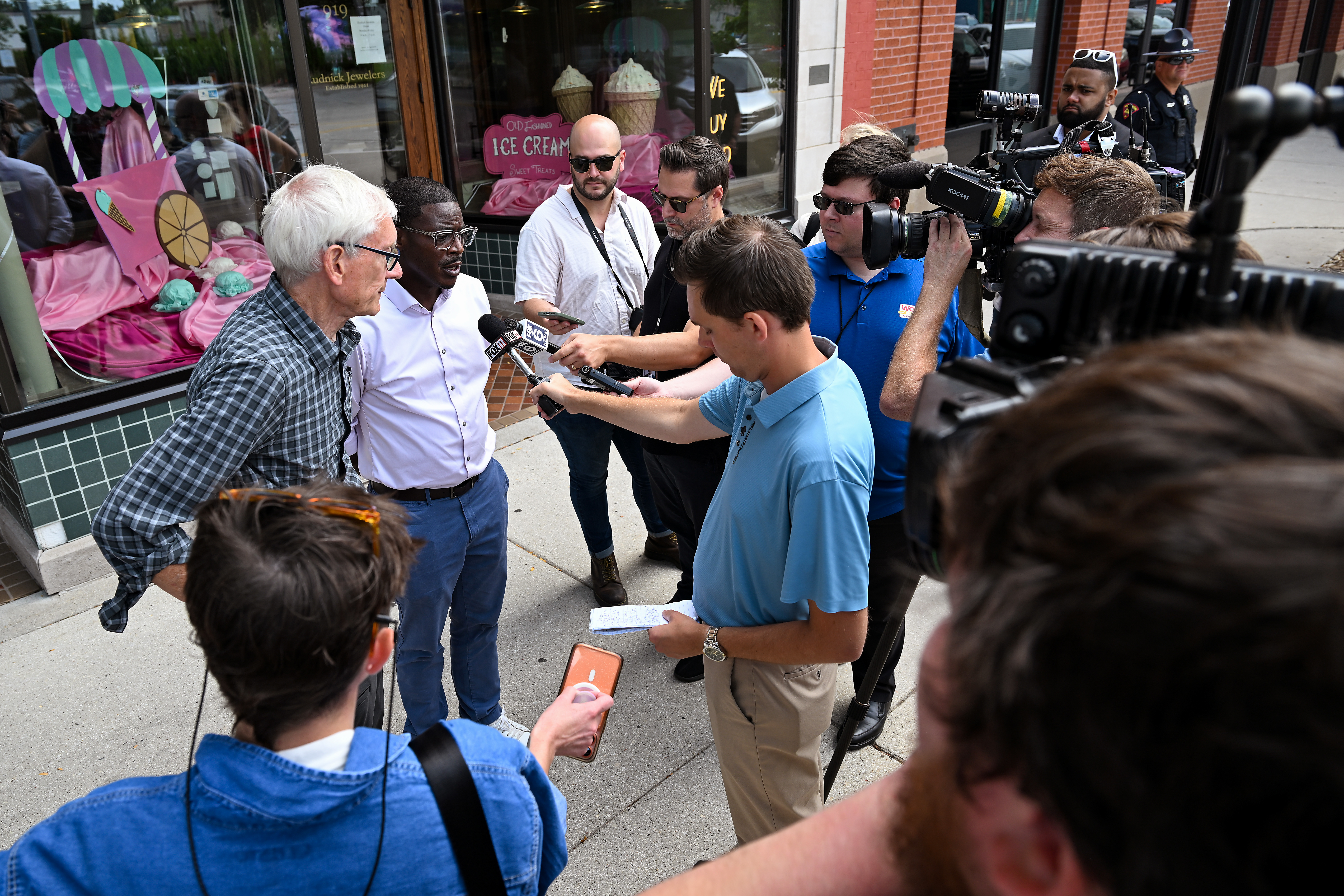 Wisconsin Gov. Tony Evers, left, and Wisconsin gubernatorial candidate David Crowley, second from left, speak to reporters during a campaign stop outside Word Haven Book House in Sheboygan, Wisconsin, on Aug. 7, 2026.