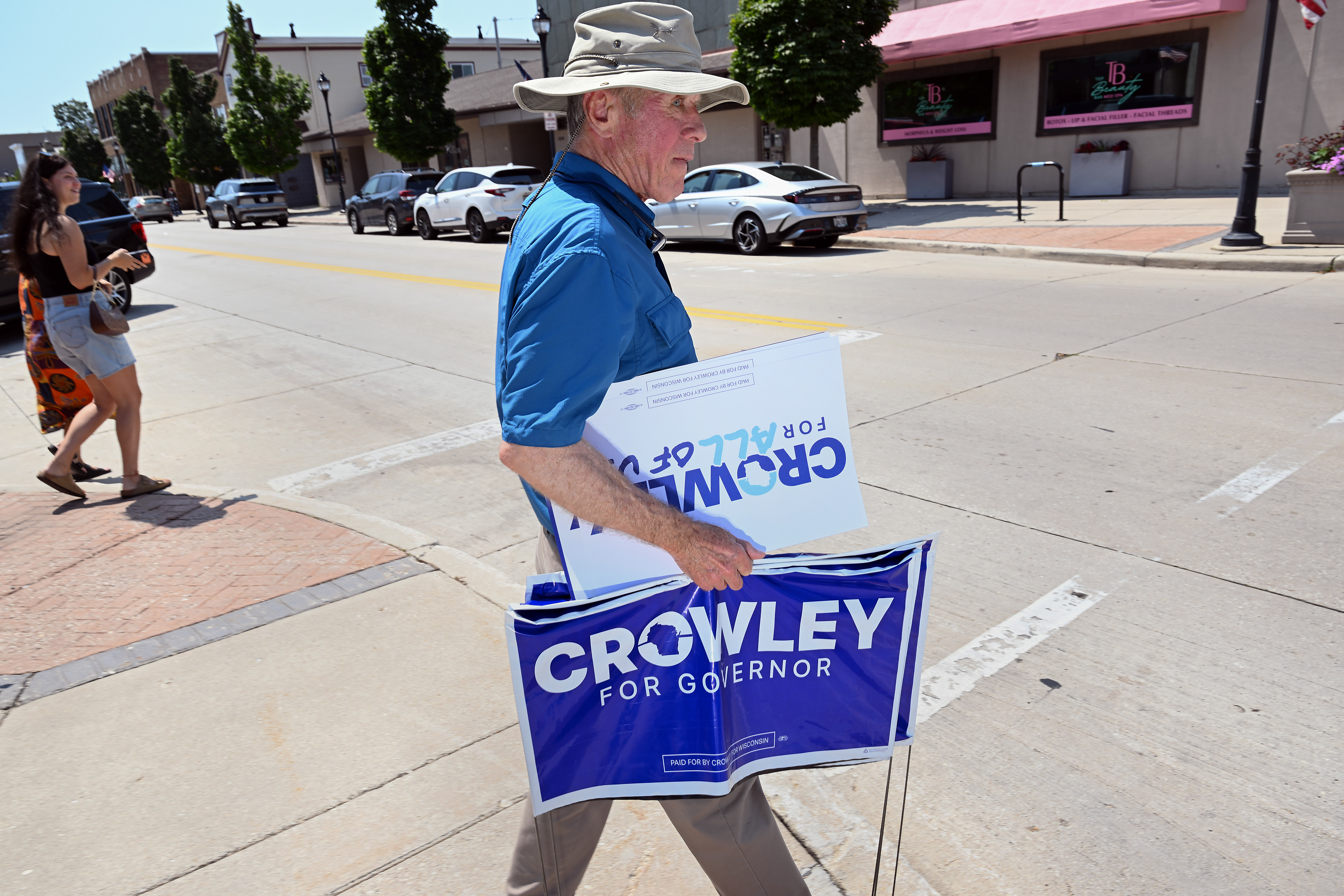 A supporter for Wisconsin gubernatorial candidate David Crowley holds campaign signs outside Urbane restaurant, where Crowley spoke during a campaign event, in Sheboygan, Wisconsin, on Aug. 7, 2026.